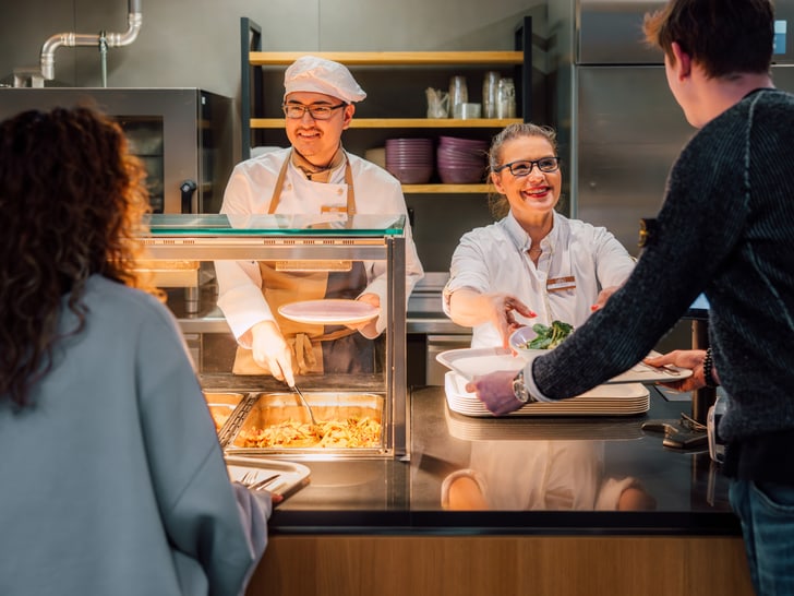 Küchenpersonal serviert Essen an Kunden in einem SV Restaurant.