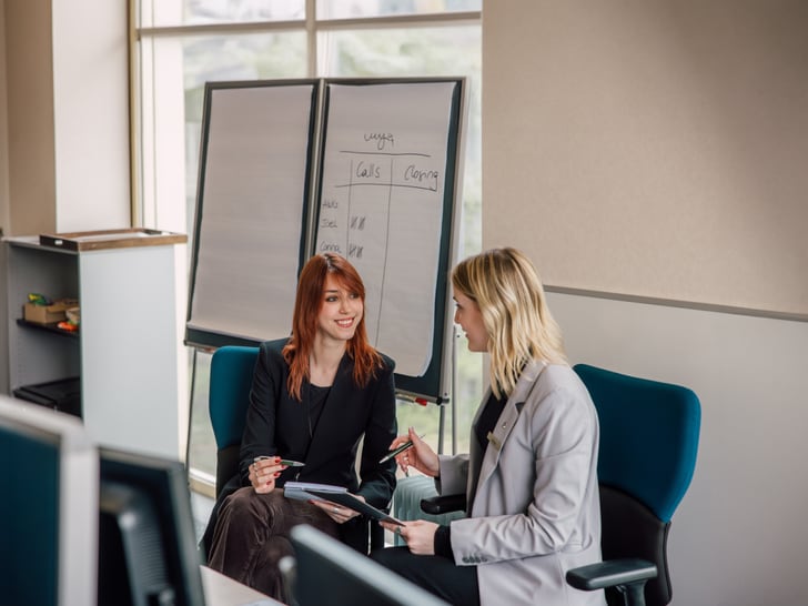 Zwei Geschäftsfrauen sprechen in einem Büro vor einem Flipchart.