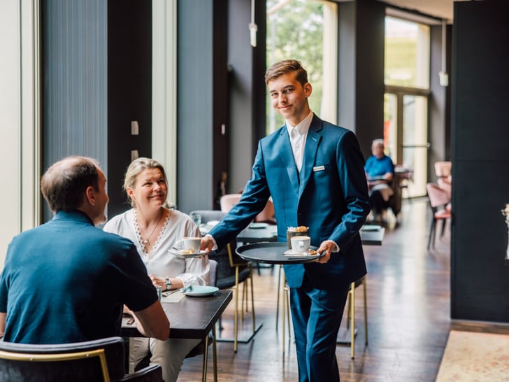 Lernender serviert Kaffee an Tisch in einem Café.
