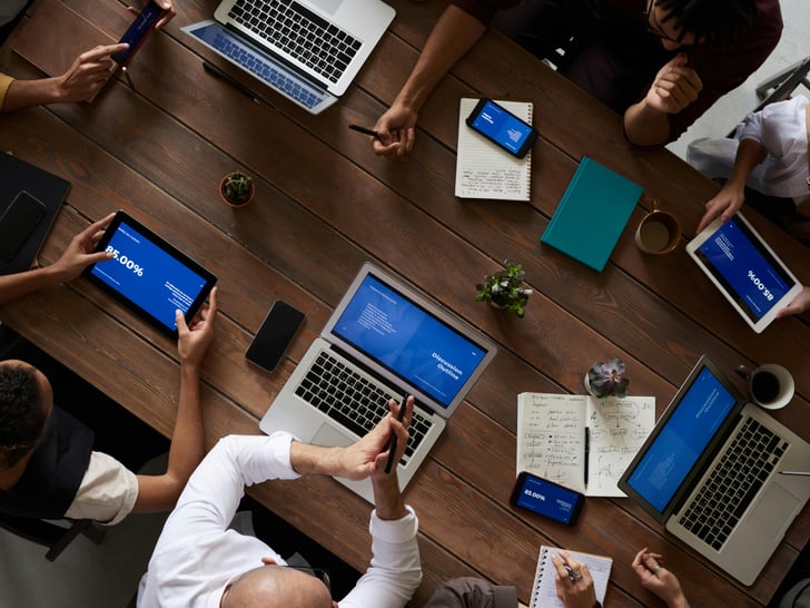 Personen sitzen an einem Tisch bei einem Meeting und haben ihre Laptops geöffnet.