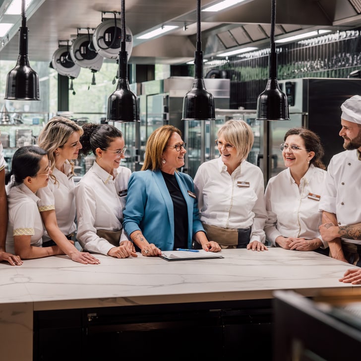 Gruppe von Köchen und Servicepersonal, die in einer Restaurantküche kommunizieren.