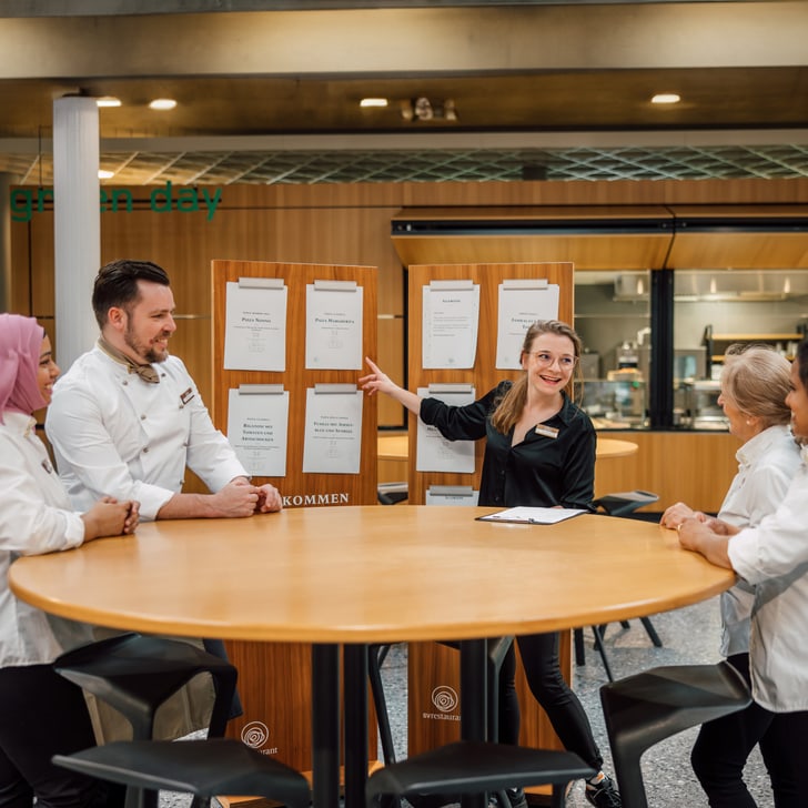 Team von Restaurantmitarbeitern bei einem Meeting am runden Tisch.