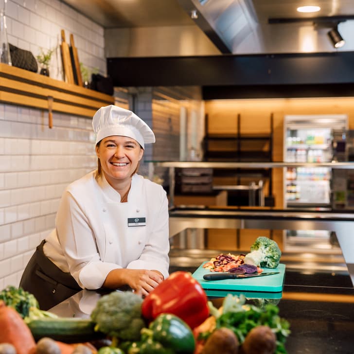 Koch mit Gemüse in moderner Küche lächelnd.