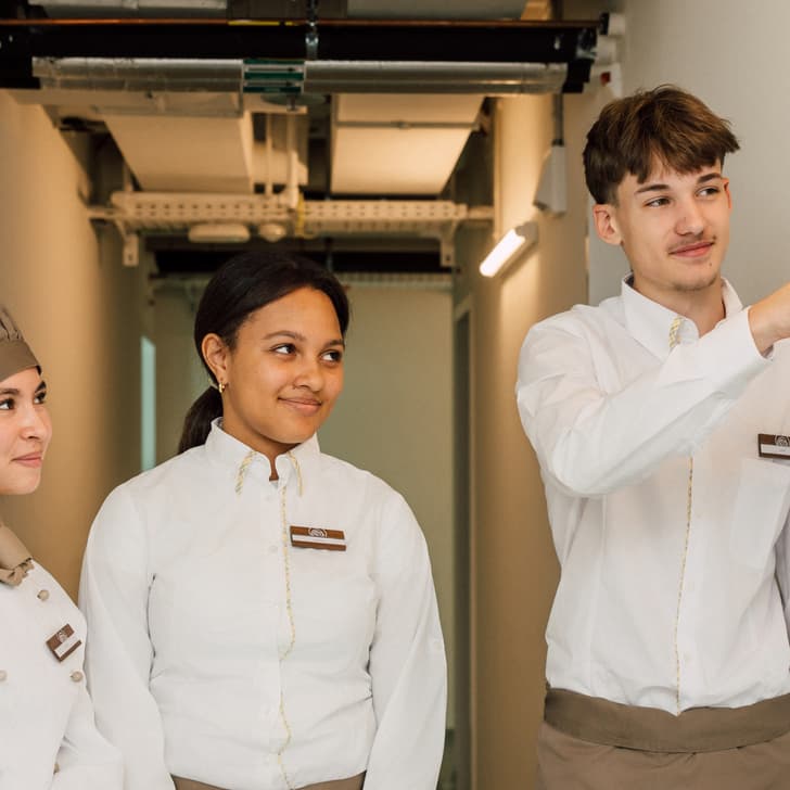 Drei Hotelangestellte betrachten ein Whiteboard im Flur.