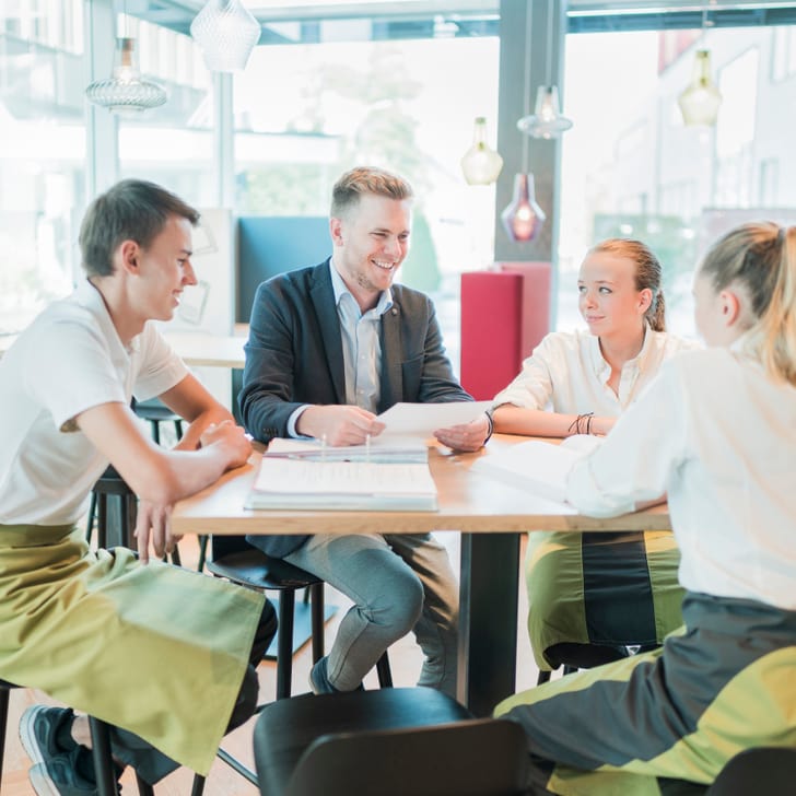 Gruppenbild Lernende mit Berufsbildner an einem Tisch