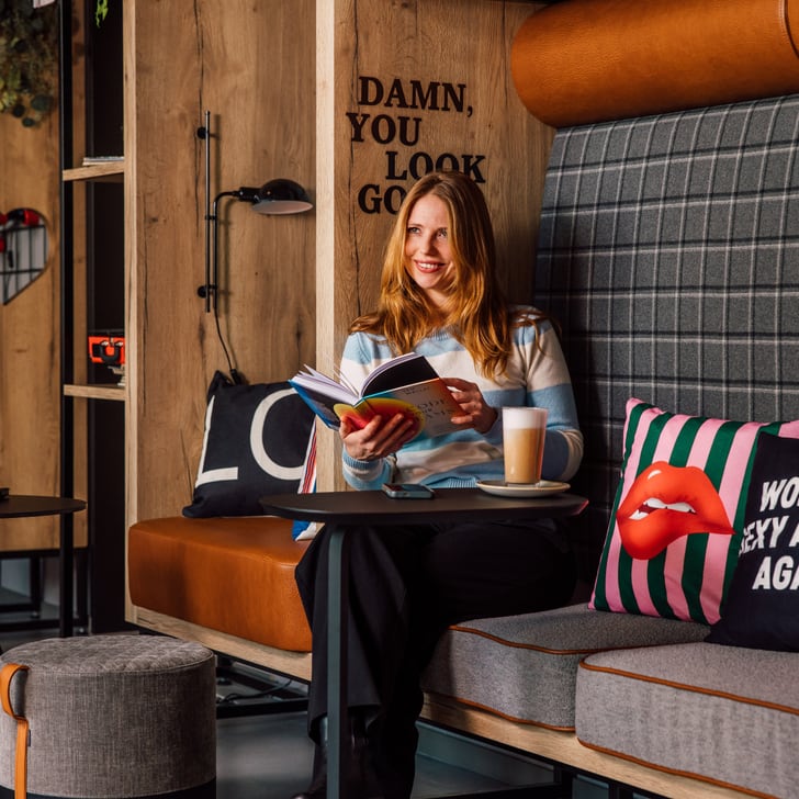 Frau liest Buch in modernem Café mit Kissen und Getränk.