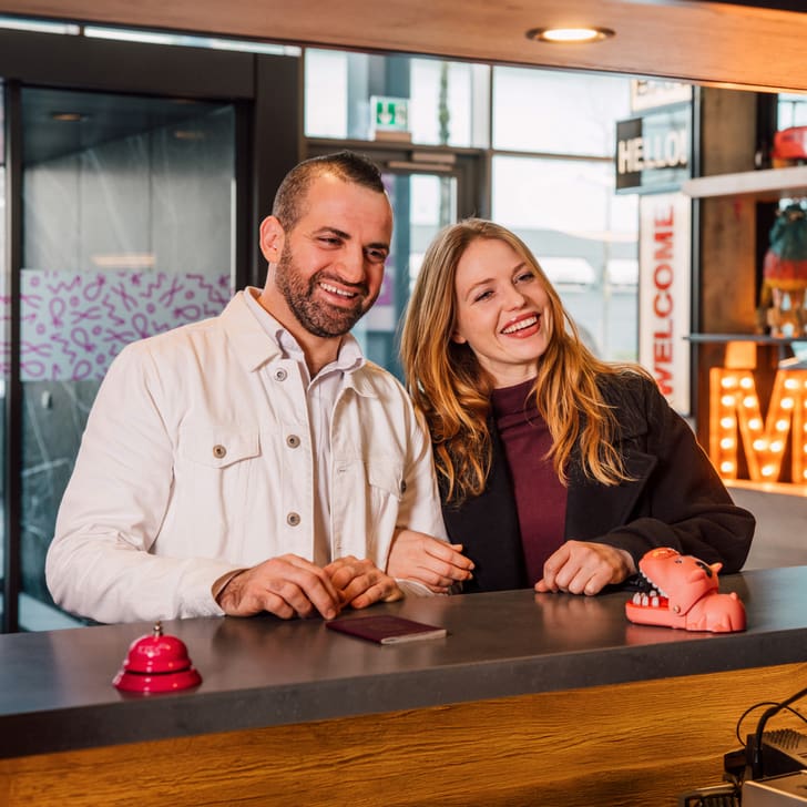 Paar lächelt an der Rezeption eines Hotels.