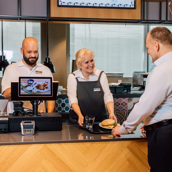 Mann an Theke wird von zwei Mitarbeitern bedient.