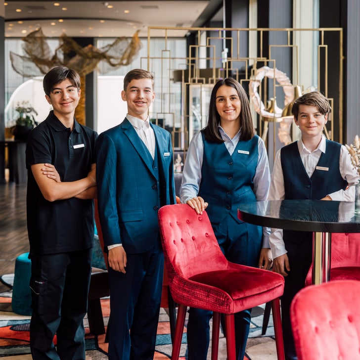 Vier Jugendliche in Restaurantuniformen posieren am Tisch in einem modernen Restaurant.