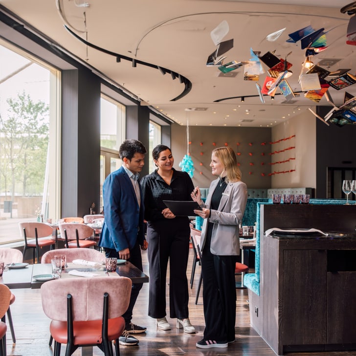 Drei Personen unterhalten sich in einem modernen Café mit Büchern an der Decke.