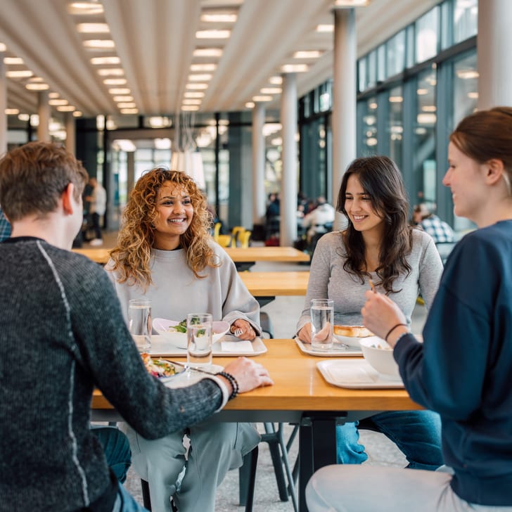 Gruppe von vier Personen sitzt und unterhält sich an einem Tisch in einer hellen Cafeteria