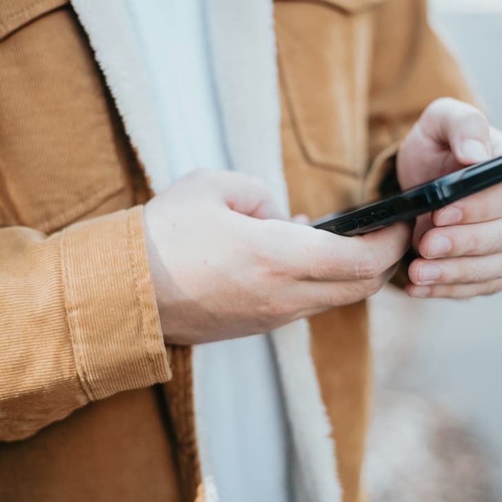 Person in brauner Jacke hält ein Smartphone.