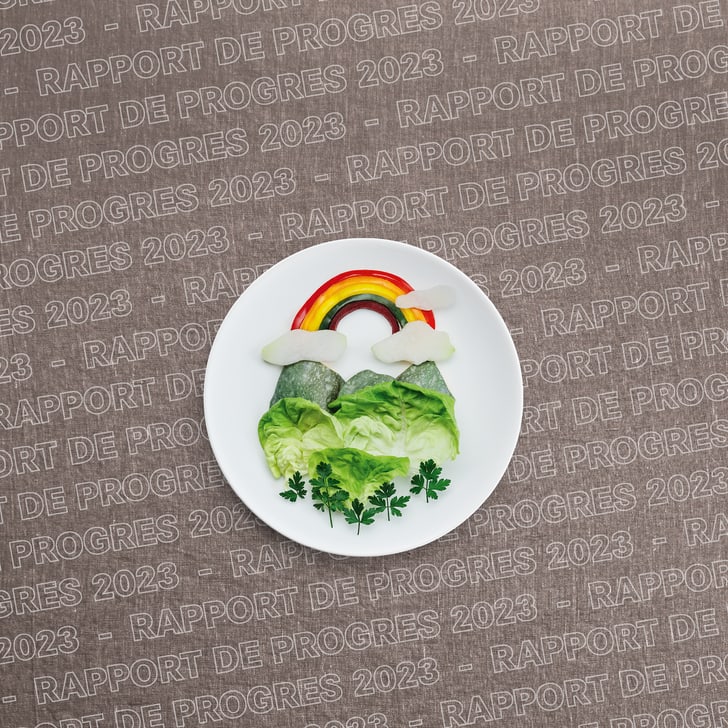 Assiette de légumes arrangée de manière créative avec un arc-en-ciel et des nuages faits de légumes sur fond imprimé.