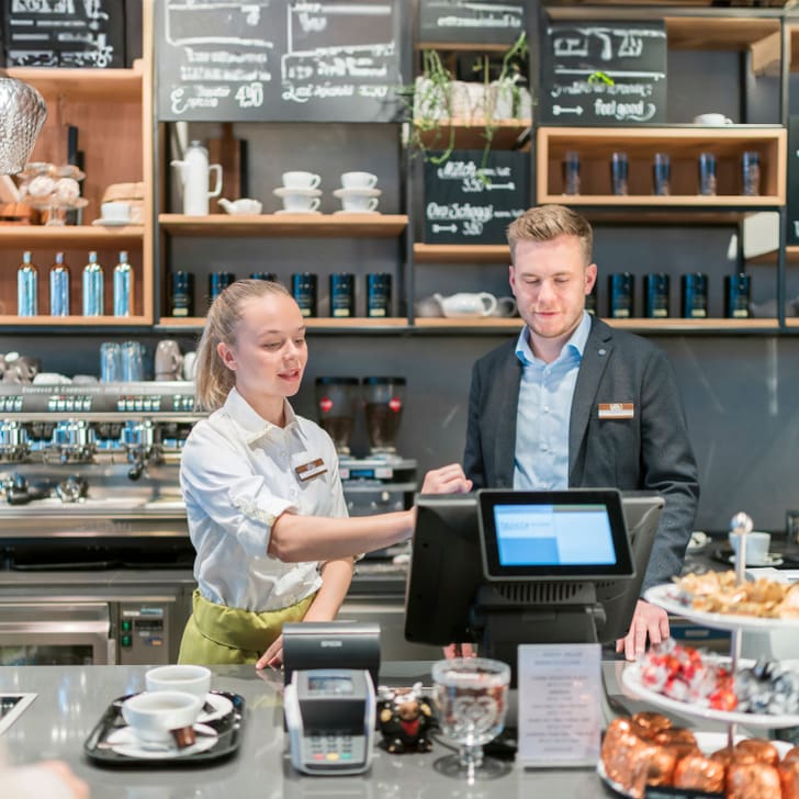 Kundenbedienung in einem modernen Café mit Theke und Kreidetafel-Menü.