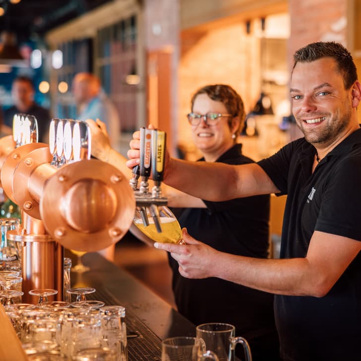 Zwei Barkeeper schenken Bier an der Theke aus, lächelnd.