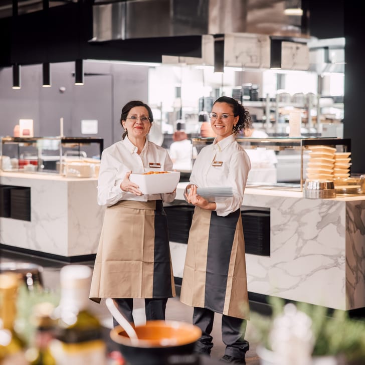 Zwei Köchinnen in einer modernen Restaurantküche mit Servierschalen.