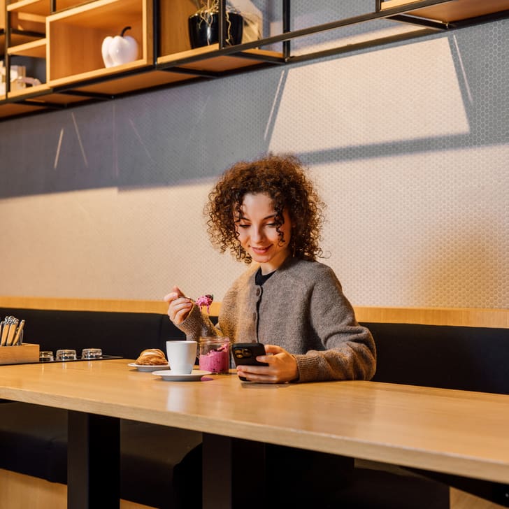 Frau trinkt Kaffee und benutzt Smartphone im Café.
