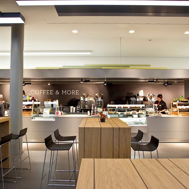 Moderne Cafeteria mit Theke und hohen Tischen.