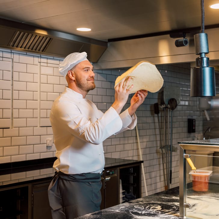 Koch wirft Pizzateig in einer Küche in die Luft.