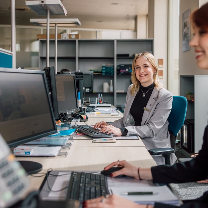 Zwei Frauen arbeiten lächelnd an Computern im Büro.