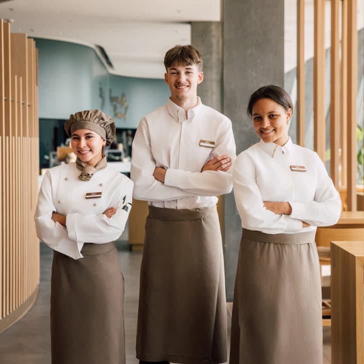 Drei lächelnde Restaurantmitarbeiter in Uniform nebeneinander stehend.