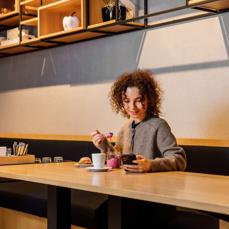Frau isst Dessert und schaut auf ihr Handy in einem Café.