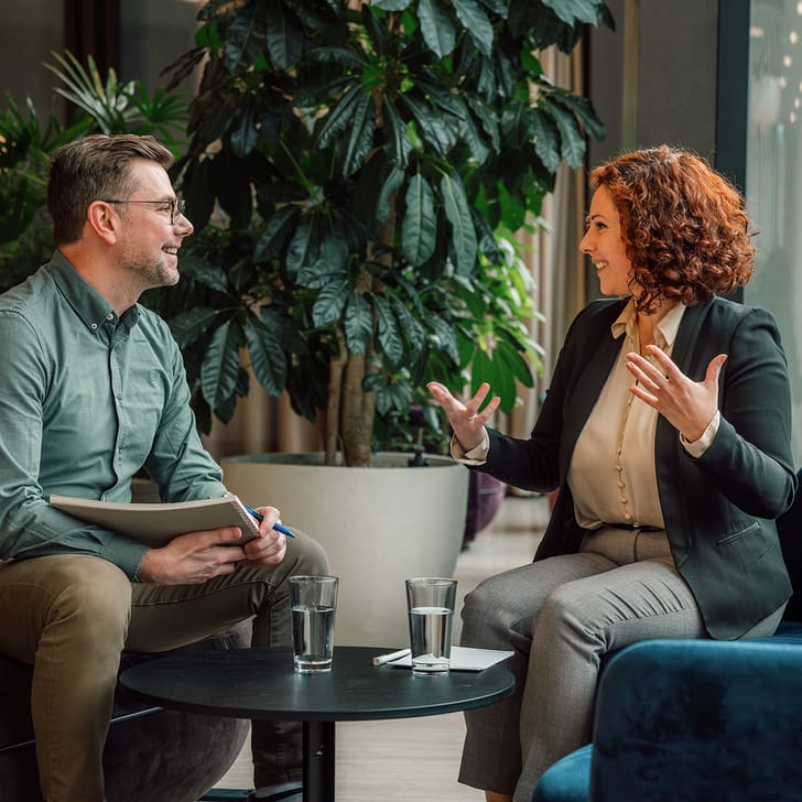 Mann und Frau bei Gespräch in modernem Büro, Pflanzen im Hintergrund.