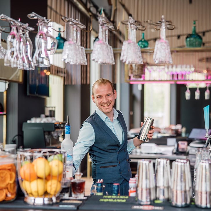 Lächelnder Barkeeper hinter einer Bar mit Cocktails und Gläsern.