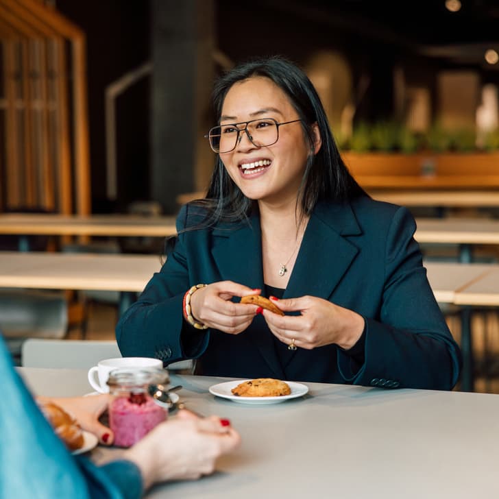 Frau lächelnd am Tisch mit Gebäck im Café sitzend.
