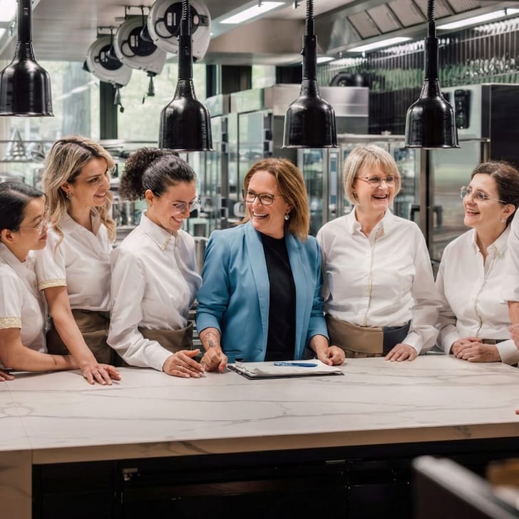 Küchenteam versammelt um einen Tisch, lächelnd, in einer modernen Küche.