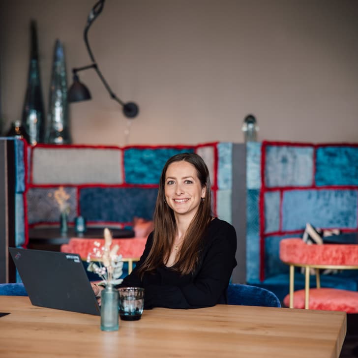 Frau sitzt an Tisch mit Laptop in modernem Café.