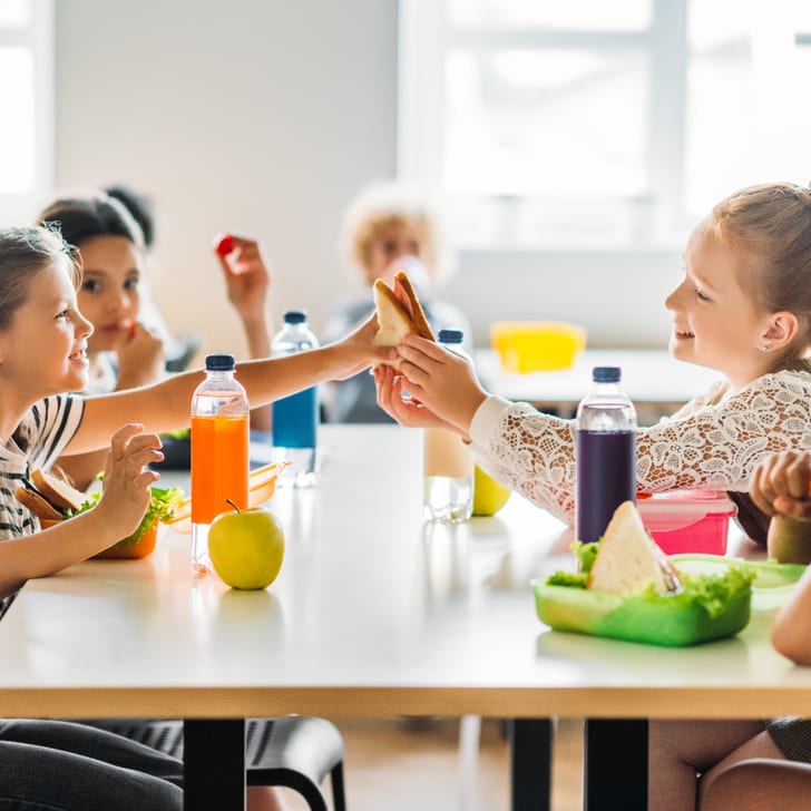 Kinder beim Essen und Händeschütteln in der Schulcafeteria.