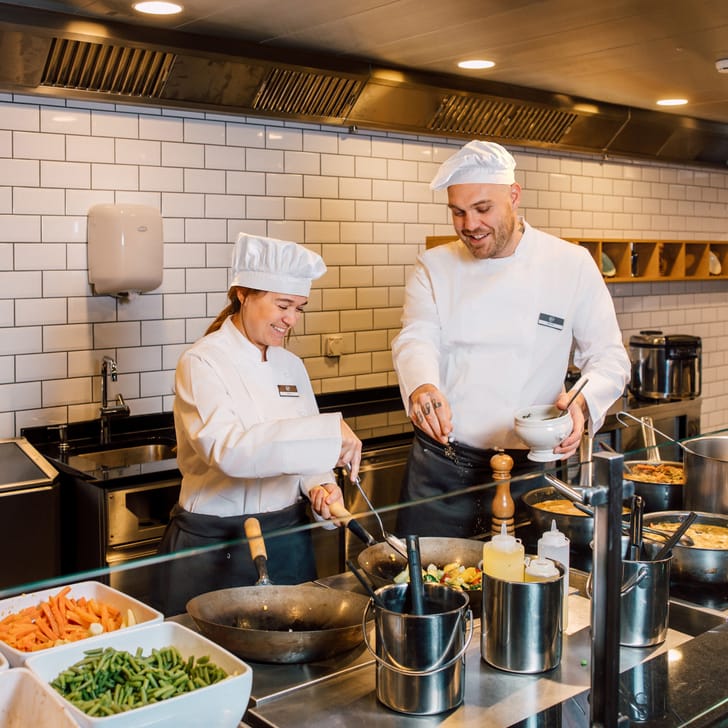 Zwei Köche in einer Restaurantküche lachen und kochen zusammen.