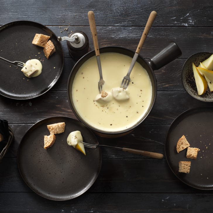 Käsefondue mit Brot und Birne auf Holztisch.