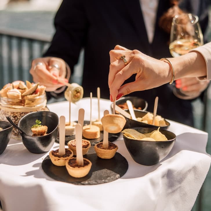 Gäste nehmen Häppchen von einem Tablett draussen auf einer Terrasse.