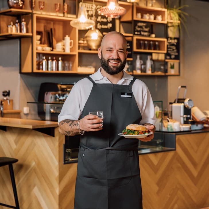 Lächelnder Kellner mit Sandwich und Getränk in Café.