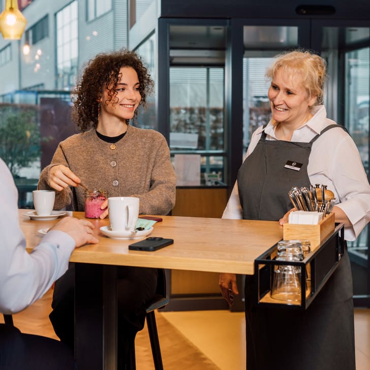 Eine Frau bedient zwei Personen an einem Café-Tisch.
