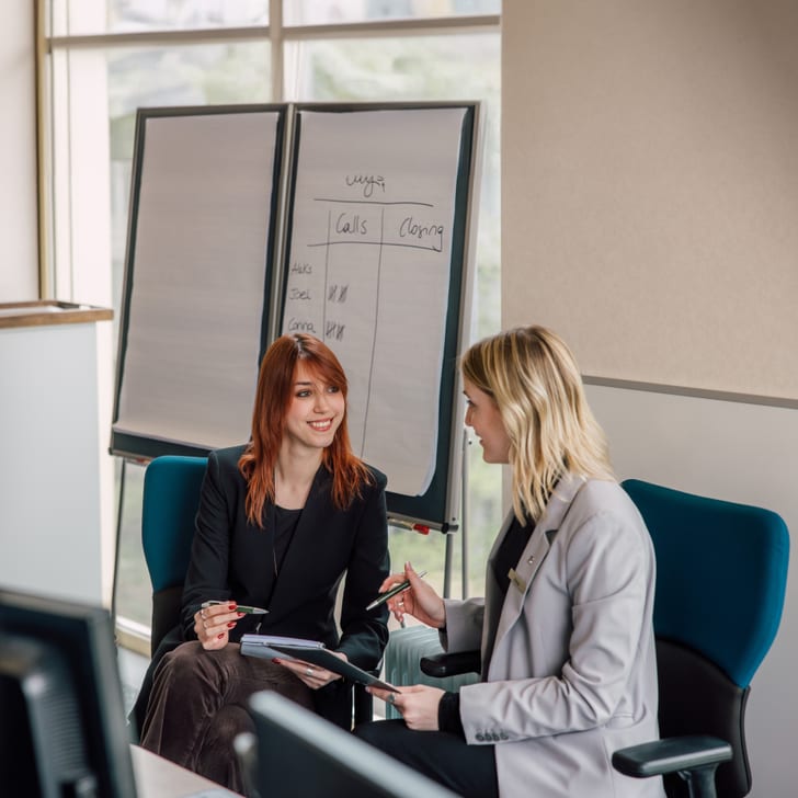 Zwei Geschäftsfrauen sprechen in einem Büro vor einem Flipchart.