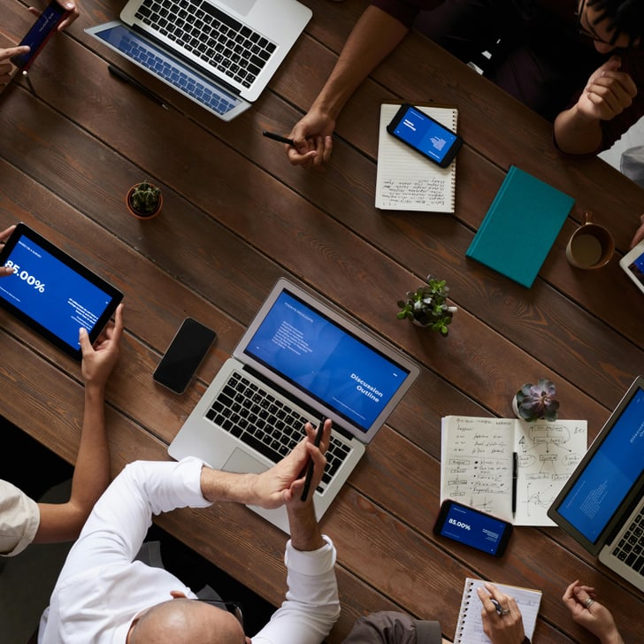 Personen sitzen an einem Tisch bei einem Meeting und haben ihre Laptops geöffnet.