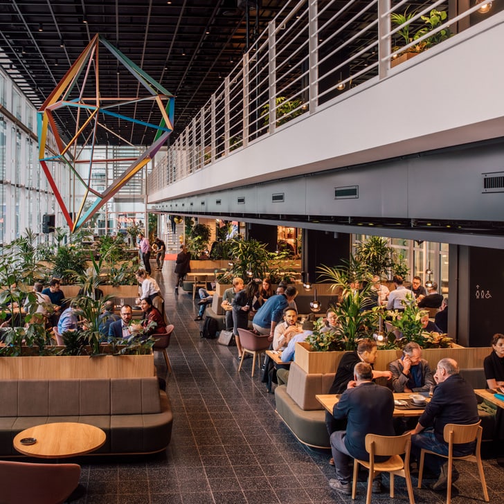 Geschäftsleute in modernem Café mit geometrischem Kunstwerk und Pflanzen.