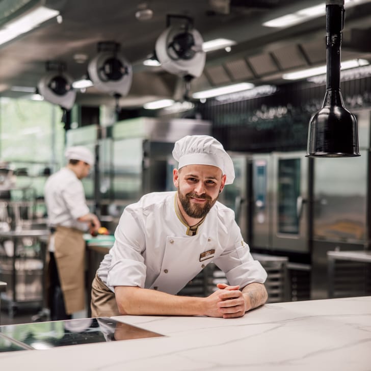 Chef in einer professionellen Küche lächelt in die Kamera",