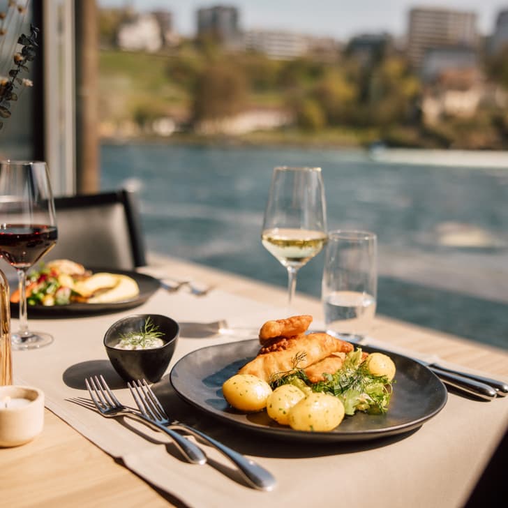 Gedeckter Tisch mit Essen und Weingläsern am Flussufer.