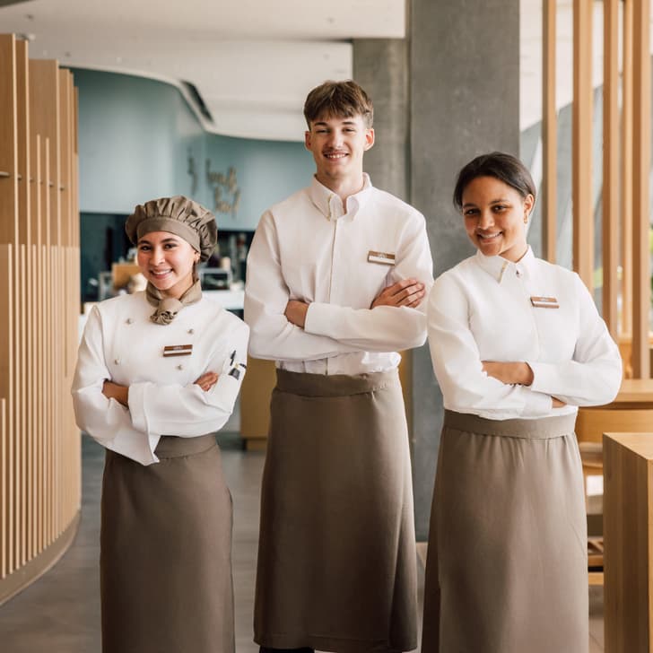 Drei lächelnde Restaurantmitarbeiter in Uniform nebeneinander stehend.