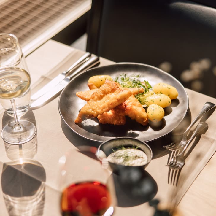 Gebratener Fisch mit Kartoffeln auf einem Teller, Wein und Wasser im Glas.