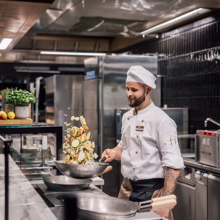 Koch in Restaurantküche wirft Gemüse in der Pfanne.