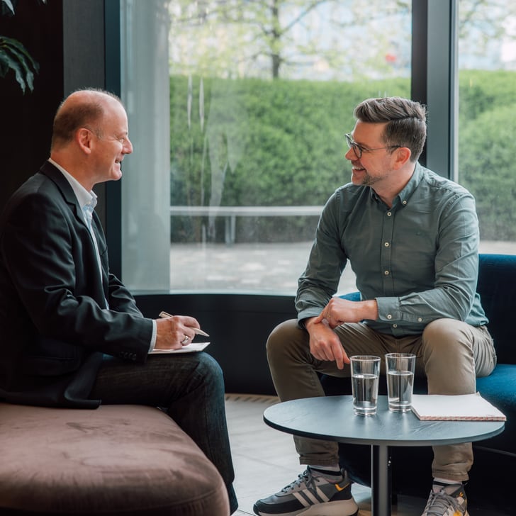 Zwei Männer sitzen und unterhalten sich in einem modernen Büro.