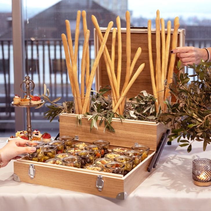 Offene Kiste mit Snacks auf Tisch, umgeben von Menschenhänden.