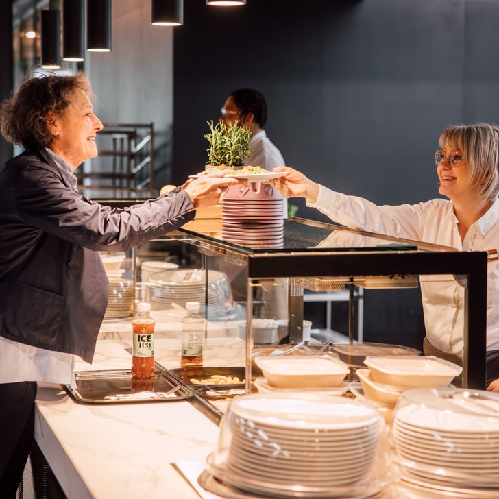 Zwei Frauen geben sich an einem Restaurantbuffet eine Pflanze.