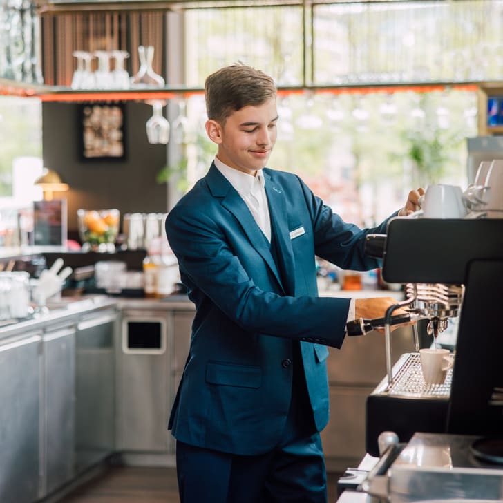 Mann in Anzug bedient Kaffeemaschine in Café.