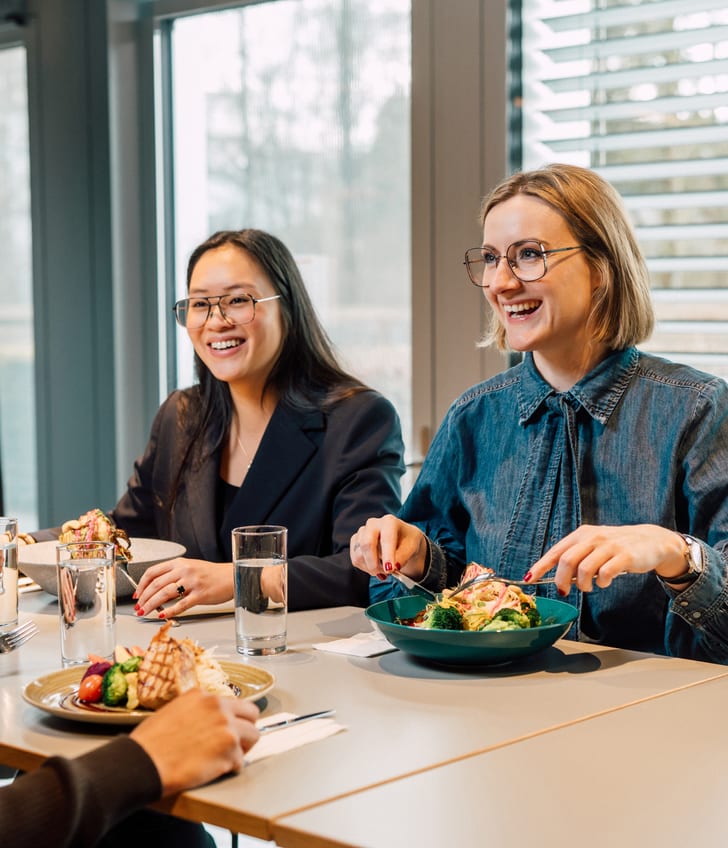Drei Personen beim Mittagessen in einem Restaurant lächelnd am Tisch.
